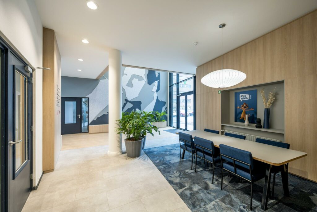 Moderne wacht- of vergaderruimte aan de Joop Geesinkweg met kunstwand, grote hanglamp en blauw meubilair.